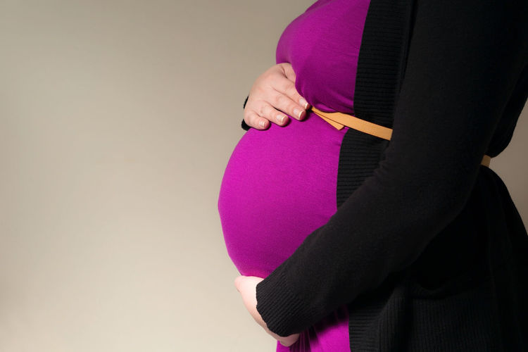 Midsection of pregnant woman standing against wall