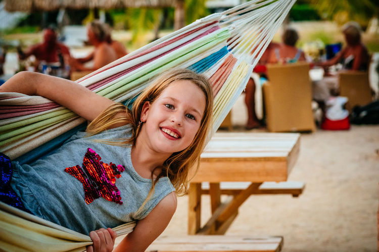 Portrait of smiling young girl woman sitting and swinging outdoors in a hammock on the beach. 