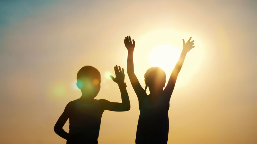 Silhouettes, figures of children, boy and girl jumping, having fun, dancing, hugging against the