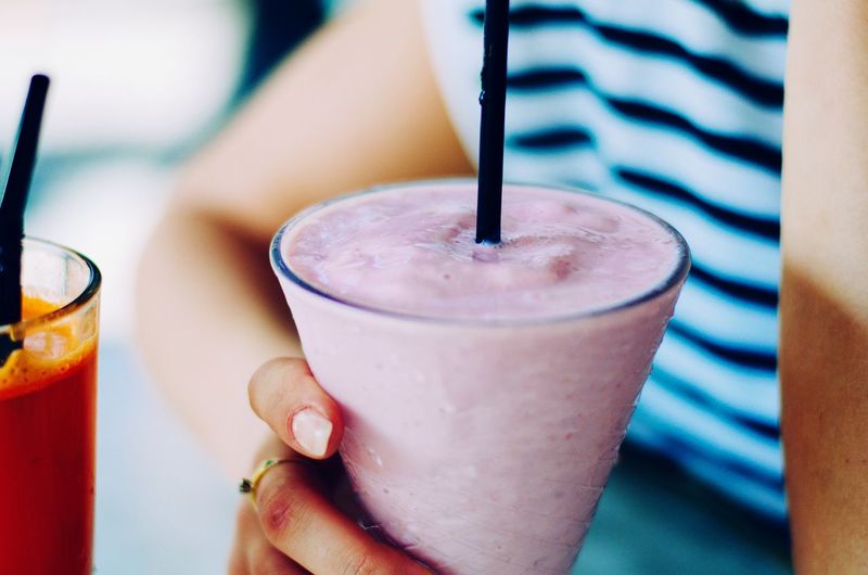 Cropped image of woman holding glass of strawberry smoothie