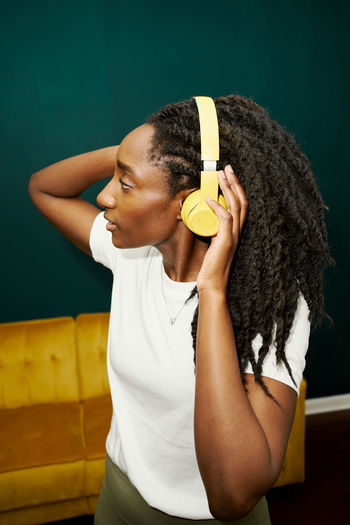 Black stylish student woman holding yellow earphones front green wall