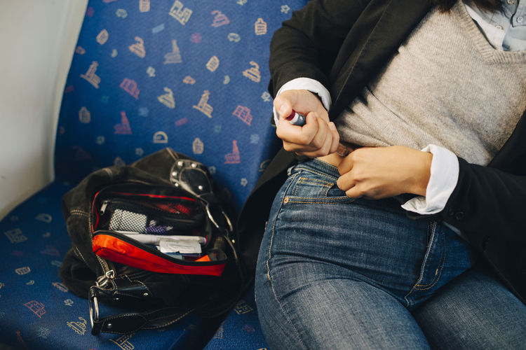 Midsection of woman injecting in abdomen while sitting in train
