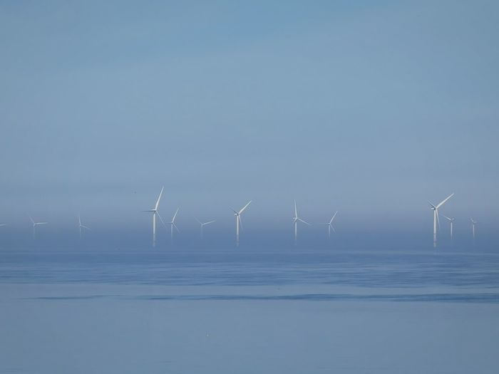 Wind turbines in sea against clear sky