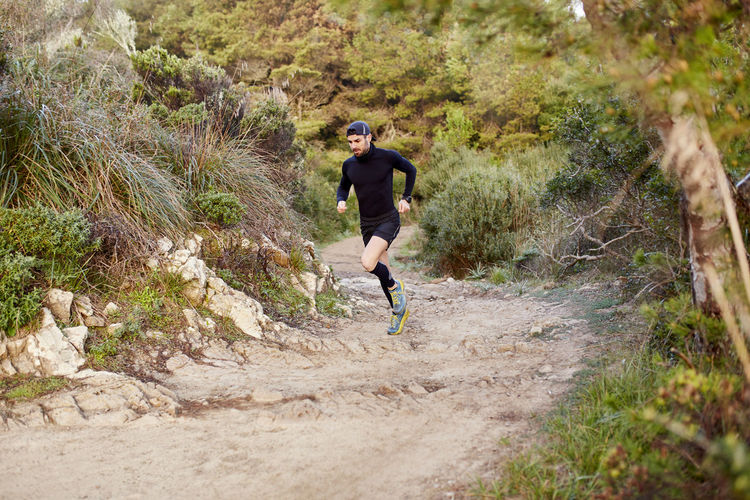 Active man running on dirt road in forest at morning
