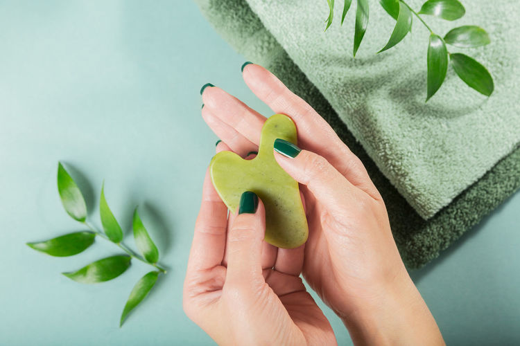 Female hand holding massage gua sha scraper for the face of green jade stone