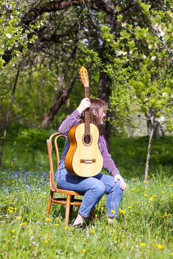 Full length of girl holding guitar sitting at park