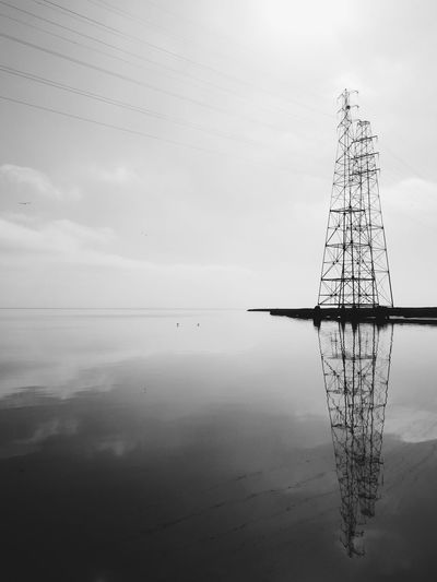 Electricity pylon reflecting on sea