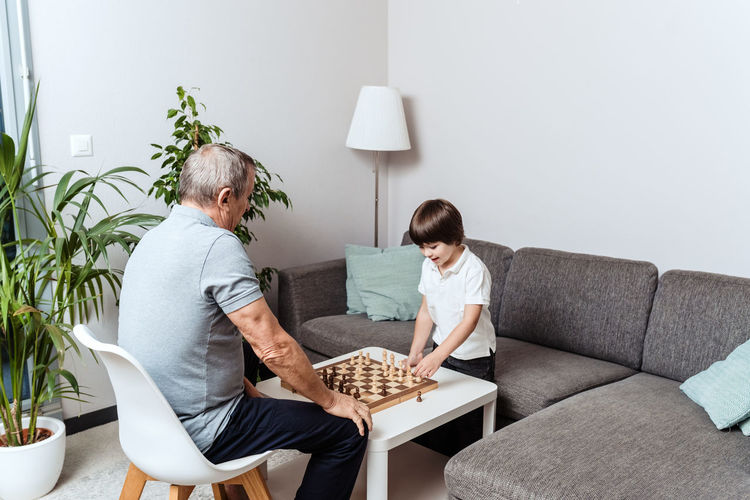 Little happy child and senior grandfather playing chess together at home. childhood hobby, education