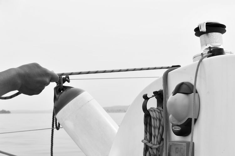 Cropped image of man holding rope on boat against clear sky