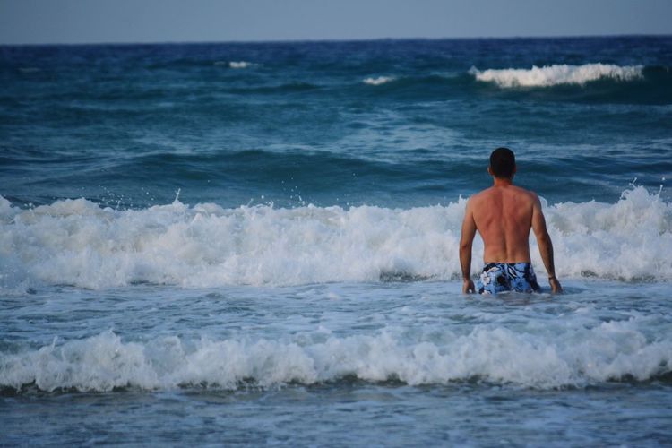 Rear view of shirtless man standing in sea against sky