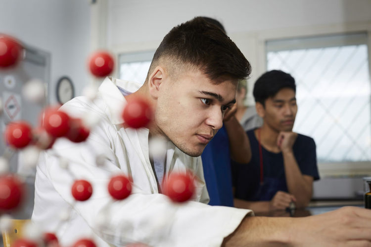 Confident young chemistry student by friends in classroom