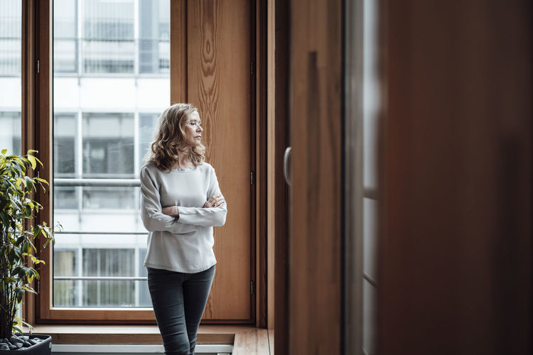 Female entrepreneur with arms crossed looking through window in office