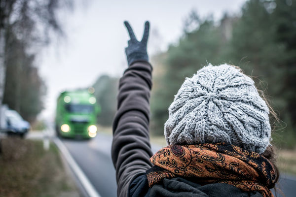 Rear view of woman wearing warm clothing while gesturing peace sign to bus on road