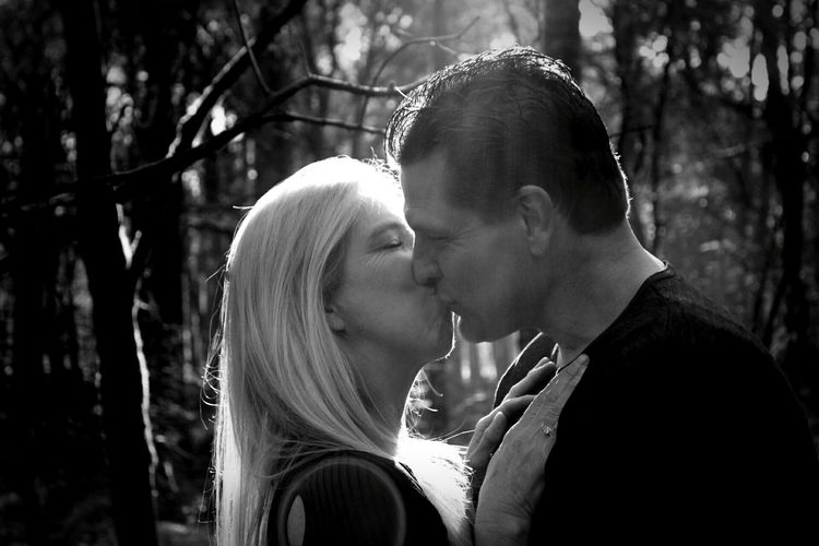 Close-up of mid adult couple kissing against trees in forest