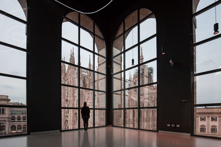 Woman looking at milan cathedral through glass window