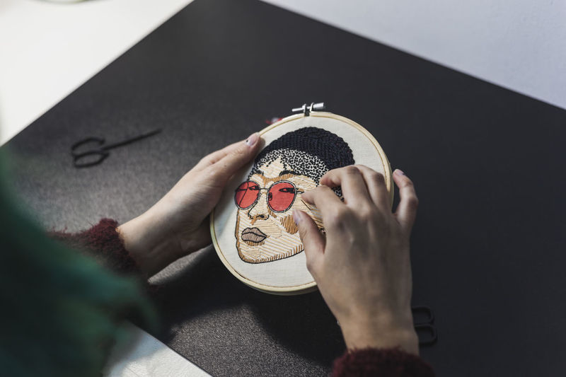 Hands of female craftsperson embroidering on cloth in frame at studio