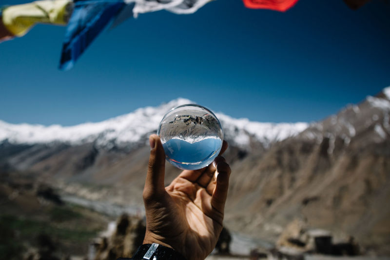 Cropped hand of man holding crystal ball against snowcapped mountain 