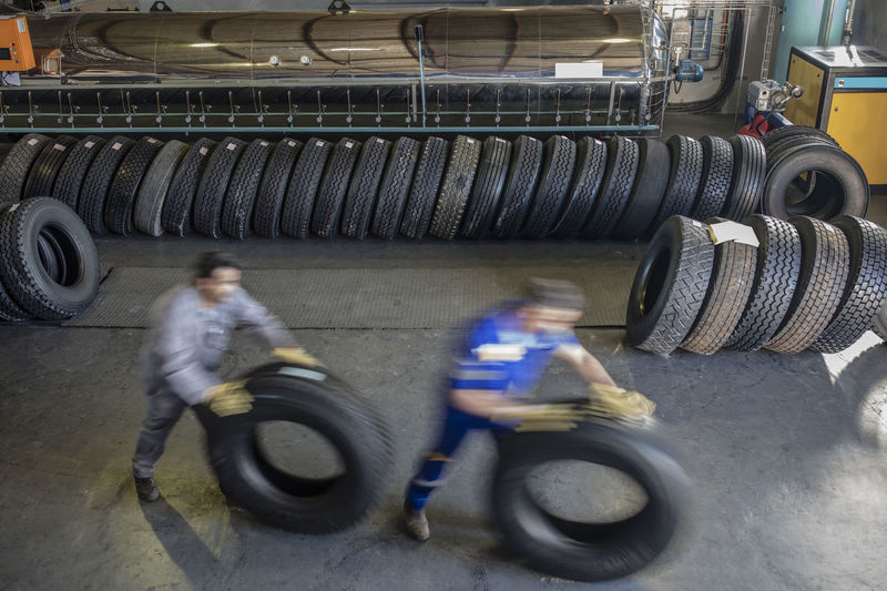 Two repairmen moving tires in factory
