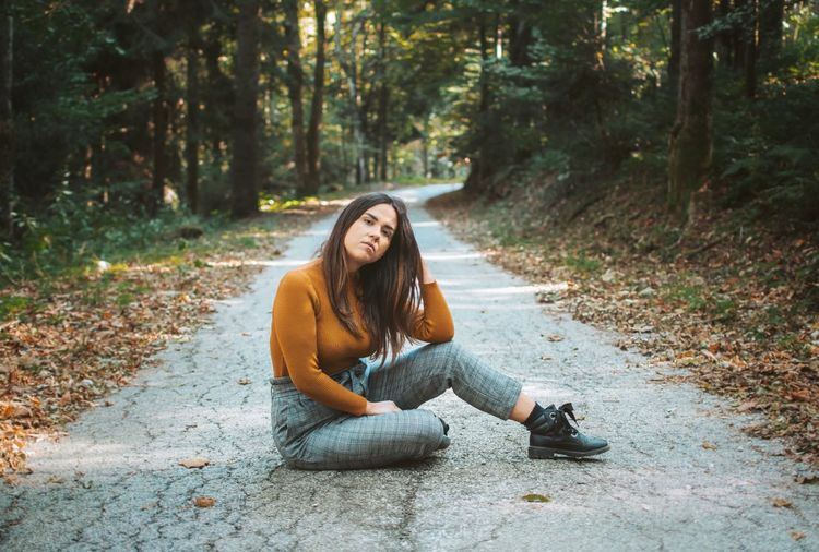 Portrait of young woman sitting on road in forest