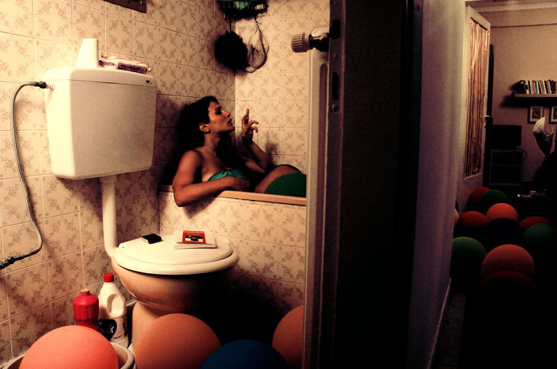 Young woman in bathtub, in house full of balloons