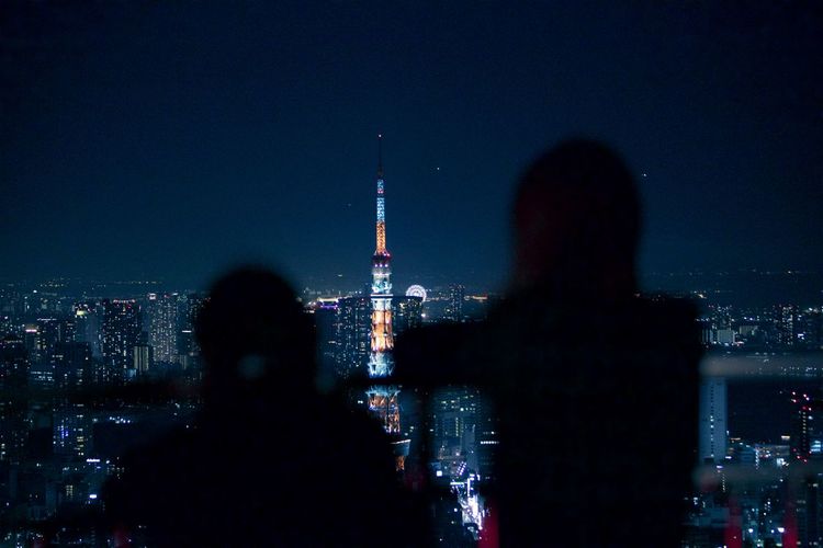 Silhouette people standing against illuminated tokyo tower in city at night