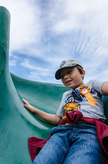 Low angle view of happy boy enjoying slide against sky