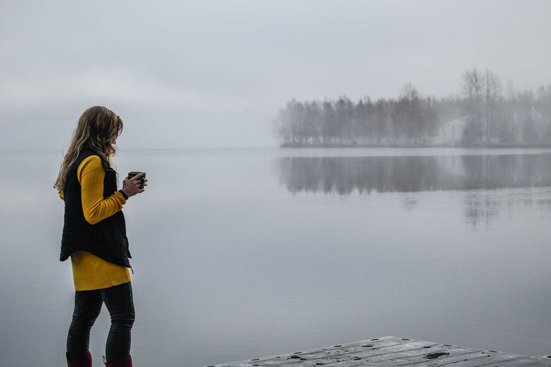 Woman standing by lake against sky during winter