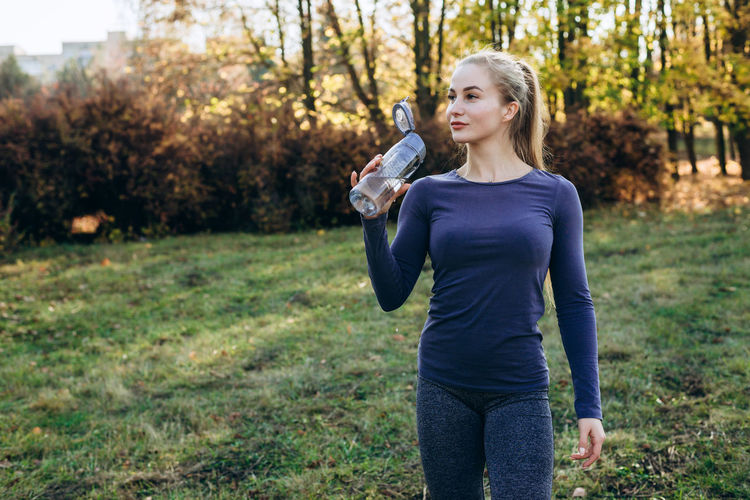 Fitness in the park, girl holds a bottle of water in her hand.