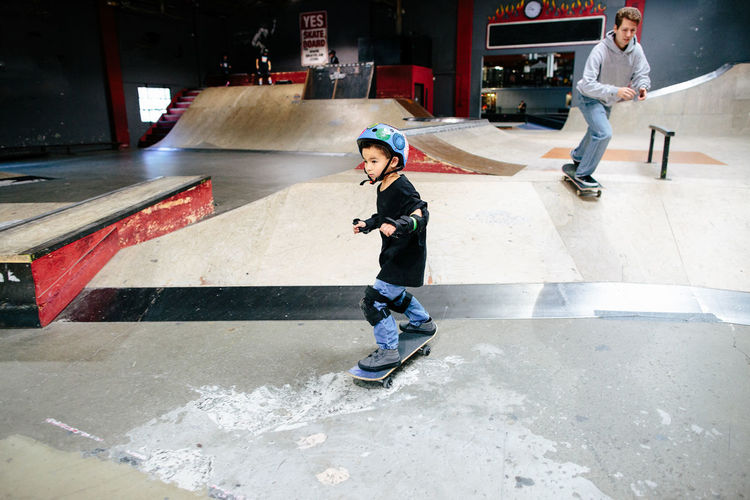 A young boy skates ahead of instructor at indoor skatepark
