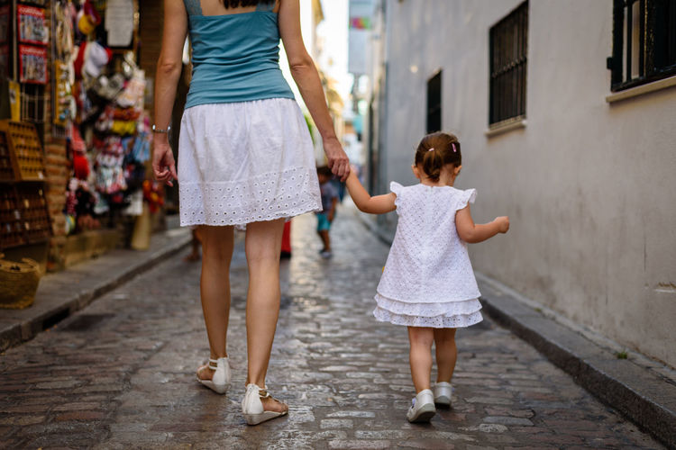 Low section of mother walking with daughter on street