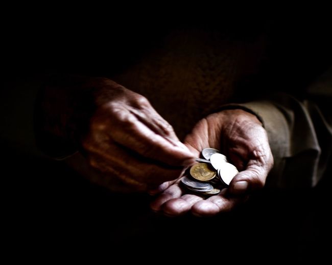 Close-up of cropped hands holding coins against black background