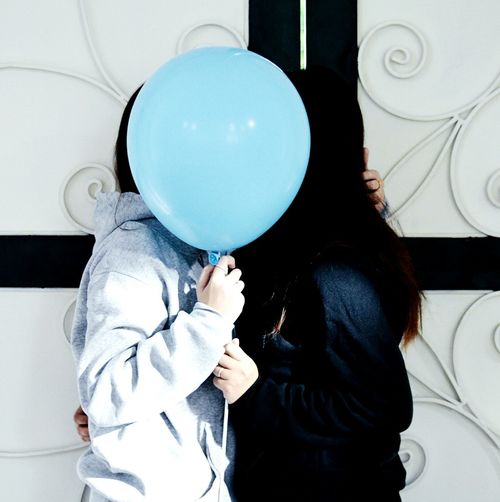 Side view of lesbian couple kissing while holding blue balloon by wall