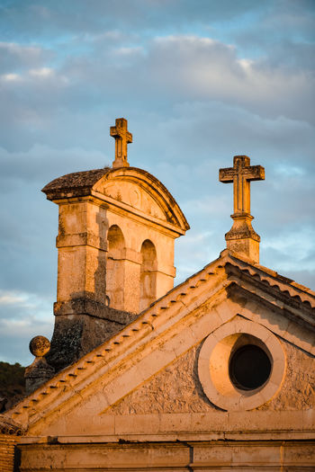Low angle detail of medieval stone church building with crosses on top against cloudy sky in cuenca town in spain