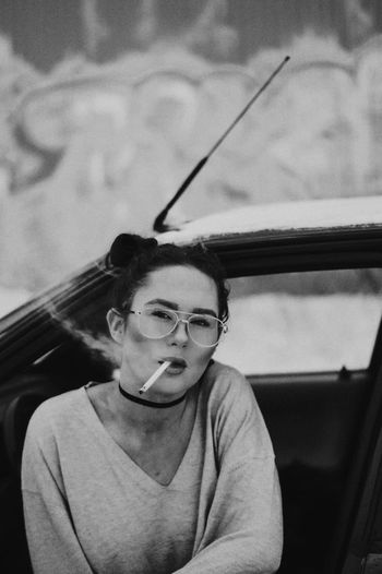 Young woman sitting on car against sky