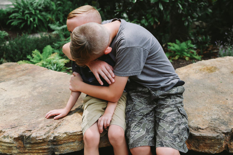 Brothers embracing while sitting on rock