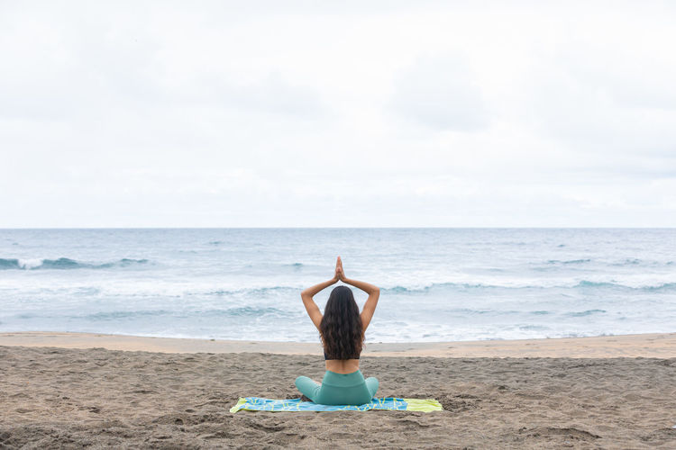 Rear view of woman standing at beach against sky
