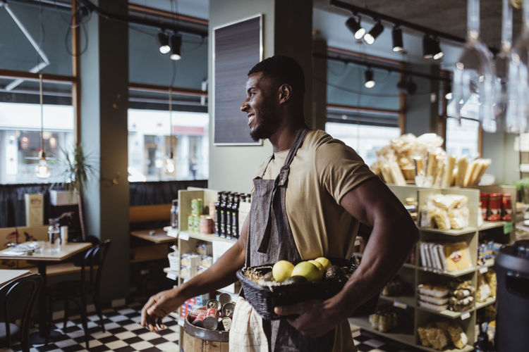 Young male owner standing with fruit basket in deli store
