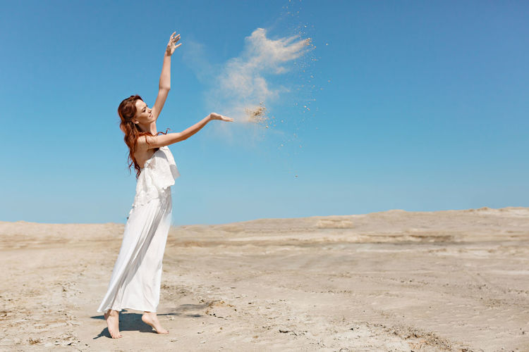 Woman with arms outstretched on sand against clear sky