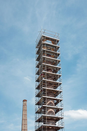 Low angle view of crane by building against sky. scaffolding on a chimney 