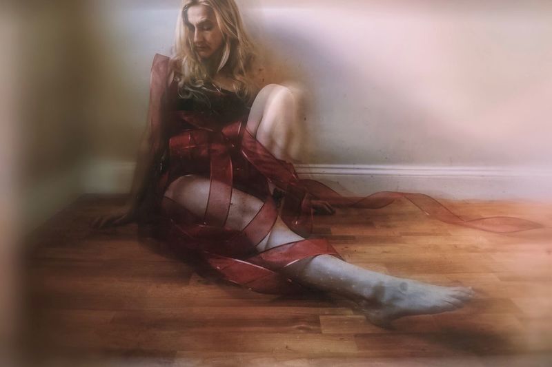 Blurred motion of woman wrapped in ribbon sitting on floor against wall