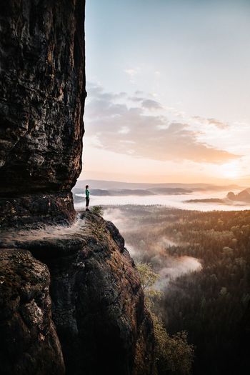 Side view of woman standing on rock against sky during sunset