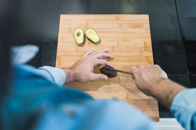 Man cooking in the kitchen in a denim shirt. an anonymous man is cutting avocados
