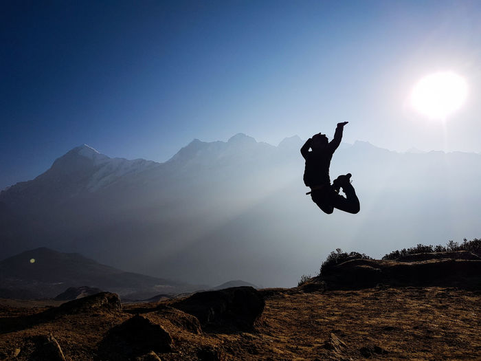 Silhouette man jumping on rock against sky