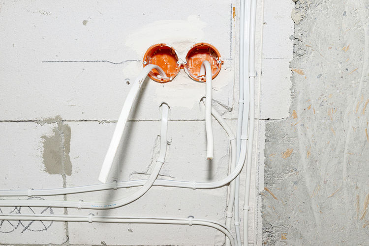 Orange, round junction box mounted in the white wall with protruding electric cables.