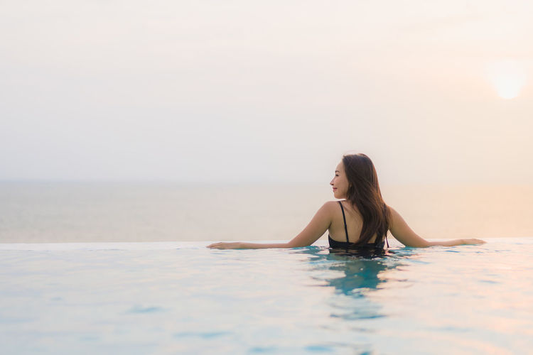 Young woman in infinity pool against sea during sunset
