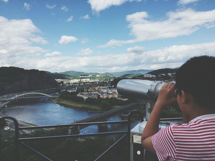 Boy looking through coin-operated binoculars at observation point by river