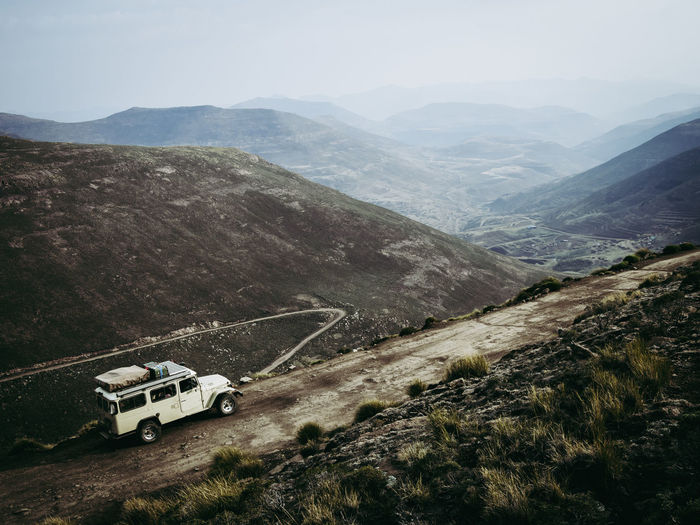 High angle view of mountain dirt road and 4x4 vehicle amidst dark landscape against sky, lesotho, africa