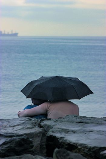 Rear view of woman with umbrella at beach against sky