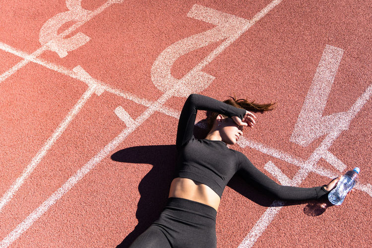High angle view of tired woman lying with water bottle on running track