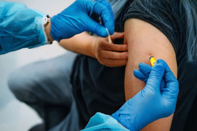Midsection of doctor giving covid-19 vaccine to woman patient
